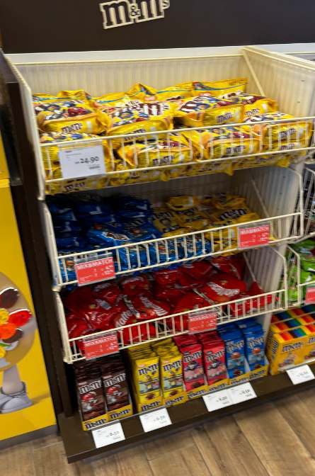 M&M’s bags in wire baskets under a small M&M’s sign at Amsterdam Schiphol